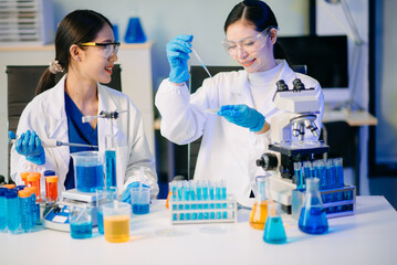 Two Asian female biotechnologists in lab coats conduct research, handle glassware, and test...