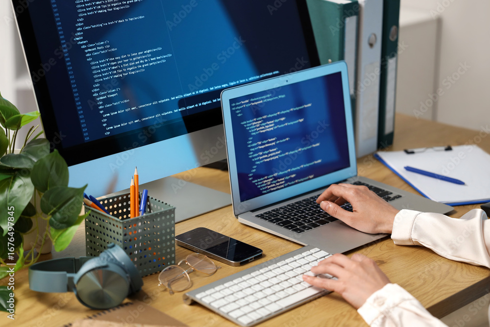 Poster female programmer's hands working with computer and laptop at table in office, closeup