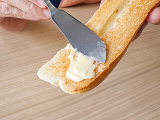Hand Holding Knife While Spreading Soft Butter on Freshly Baked Baguette Slice