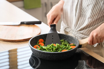 Woman with spatula frying tasty vegetables in kitchen, closeup