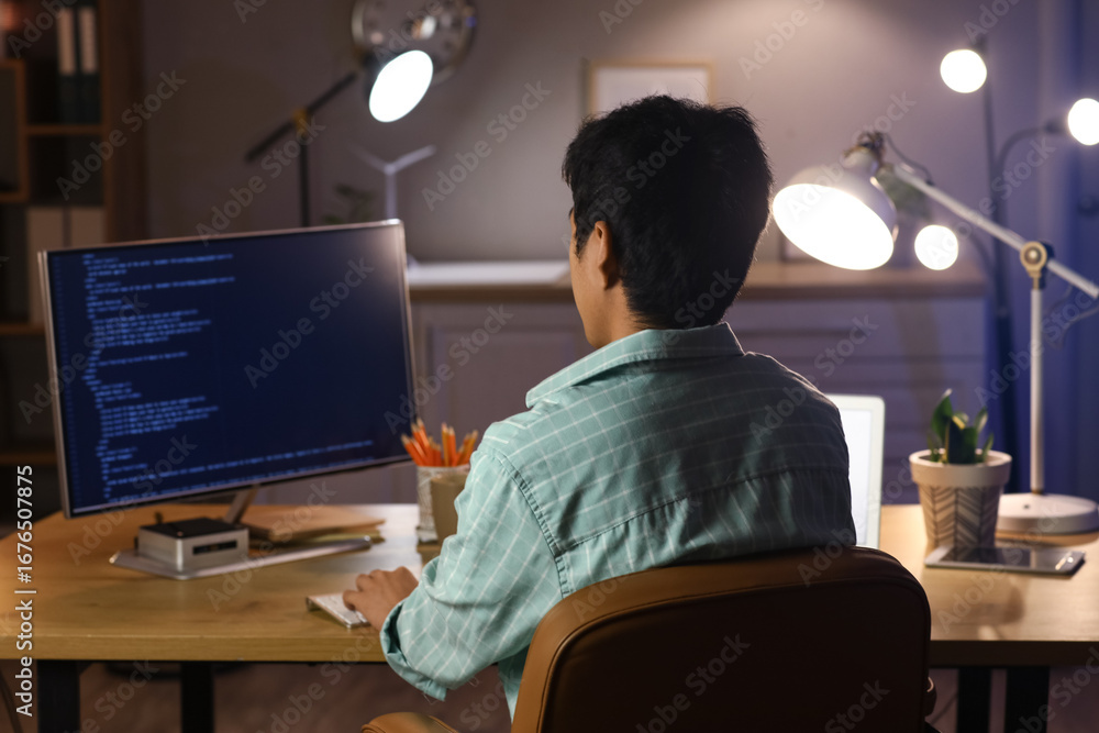 Poster male programmer working with computer in office at night, back view
