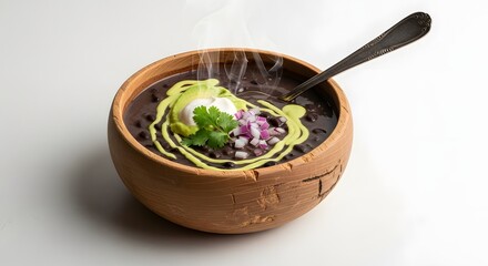 A steaming hot bowl of black bean soup in a rustic clay bowl, garnished with avocado crema, red onion, and cilantro.