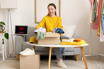 Young woman packing clothes into box for donation at home