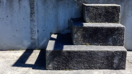 A set of dark gray stone steps cast dramatic shadows against a light gray concrete wall.