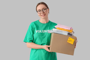 Female volunteer with box of clothes for donation on light background