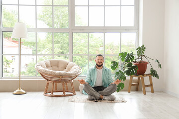 Handsome man meditating near cocoon chair at home