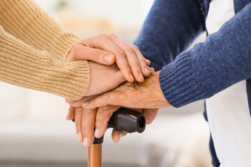Woman and grandmother with stick holding hands at home, closeup. Care concept