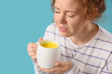 Young redhead woman with turmeric drink on blue background, closeup