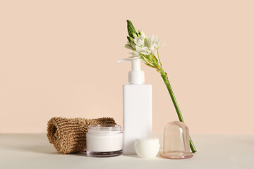Vacuum jar for anti-cellulite massage with loofah and cosmetic products on table near beige wall