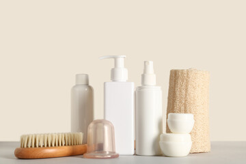 Vacuum jar with brush for anti-cellulite massage and cosmetic products on table near light wall