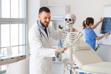 Fototapeta premium Male doctor examining arm bone of human skeleton model in clinic