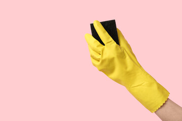 Hand in rubber glove holding sponge for cleaning on pink background