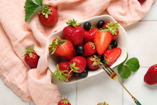 Bowl with fresh ripe strawberries and blueberries on white tile background