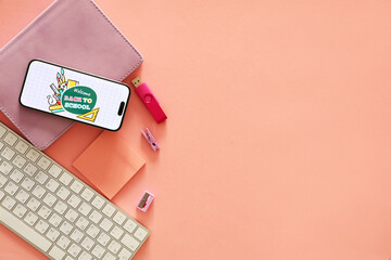 Mobile phone with text WELCOME BACK TO SCHOOL, computer keyboard and stationery on pink background