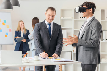 Young businessman using VR glasses with his colleague in office