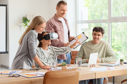 Young woman using VR glasses with her colleagues at table in office