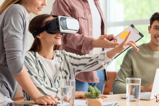 Young woman using VR glasses with her colleagues at table in office