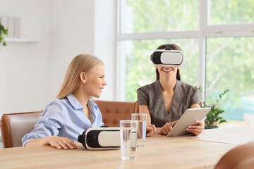 Young businesswoman with tablet computer using VR glasses and her colleague in office