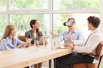 Young businessman using VR glasses with his colleagues at table in office