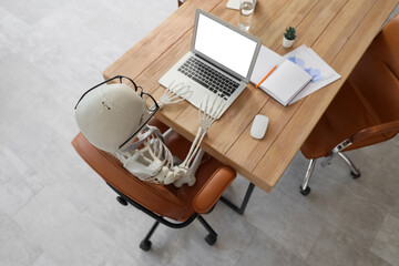 Human skeleton model at desk in office