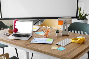 Table with blank laptop, headphones and sticky notes prepared for business meeting in conference...