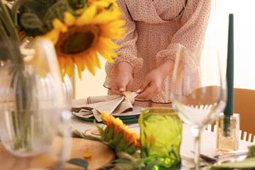 Young woman decorating served dining table with beautiful sunflowers and folded napkins