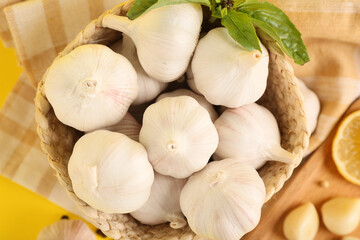 Wicker basket with fresh garlics and basil leaves on yellow background