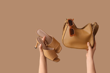 Female hands with handbag, shoes and sunglasses on beige background