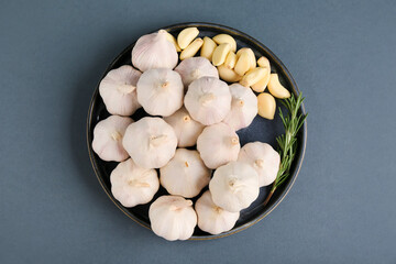 Plate with fresh garlics and rosemary on grey background