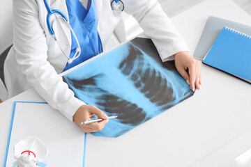 Female doctor with x-ray image of lungs at table in clinic, closeup