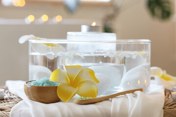 Sea salt with spa stones, candles and plumeria flowers on wicker table in salon