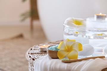 Sea salt with spa stones, candles and plumeria flowers on wicker table in salon
