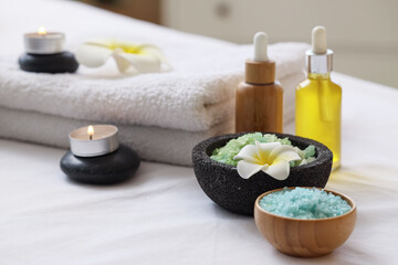 Towels with candles, spa stones, cosmetic oil, sea salt and plumeria flowers on couch in salon