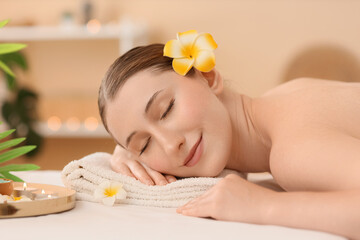 Beautiful young happy woman with yellow plumeria flowers lying on couch in spa salon