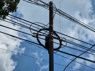 Utility pole with multiple electrical wires and coiled cables against a bright cloudy sky