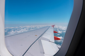 View of airplane wing above clouds during flight on clear day with blue sky