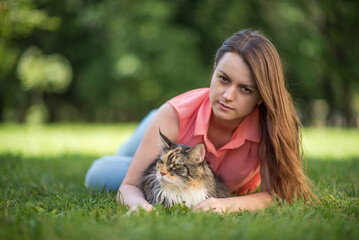 Portrait of a young beautiful girl with a Maine Coon cat in a summer park.