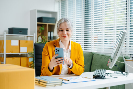 Startup small business SME, Entrepreneur owner woman using smartphone or tablet taking receive and checking online purchase shopping order to preparing pack product box.