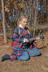 Portrait of smiling caucasian girl plays ukulele in autumnal park. Young woman plays guitar musical...