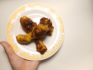Ayam Kecap, or chicken cooked with sweet soy sauce. One chicken drumstick on white plate,