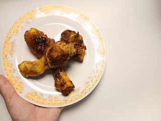 Ayam Kecap, or chicken cooked with sweet soy sauce. One chicken drumstick on white plate,