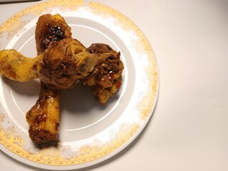 Ayam Kecap, or chicken cooked with sweet soy sauce. One chicken drumstick on white plate,