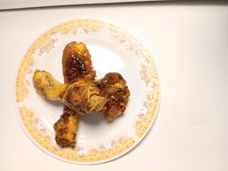 Ayam Kecap, or chicken cooked with sweet soy sauce. One chicken drumstick on white plate,
