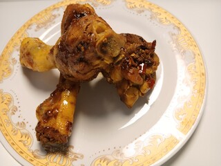 Ayam Kecap, or chicken cooked with sweet soy sauce. One chicken drumstick on white plate,