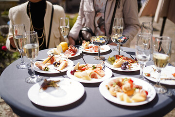 Outdoor catering table with assorted appetizers, cheese, fruits, cured meats, and champagne glasses during social gathering.