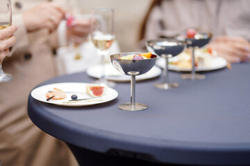 Outdoor catering table with assorted appetizers, cheese, fruits, cured meats, and champagne glasses during social gathering.