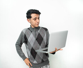 Joven hombre sosteniendo una laptop color gris con una mano en su cintura en un fondo blanco aislado
