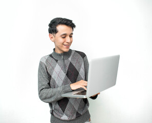 Joven hombre sonriendo mientras sostiene y usa una laptop gris