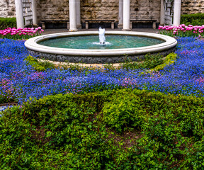 A small fountain in the park among the flowers in summer.