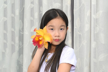 Portrait of a cute little Asian girl with a colourful Cattleya orchid